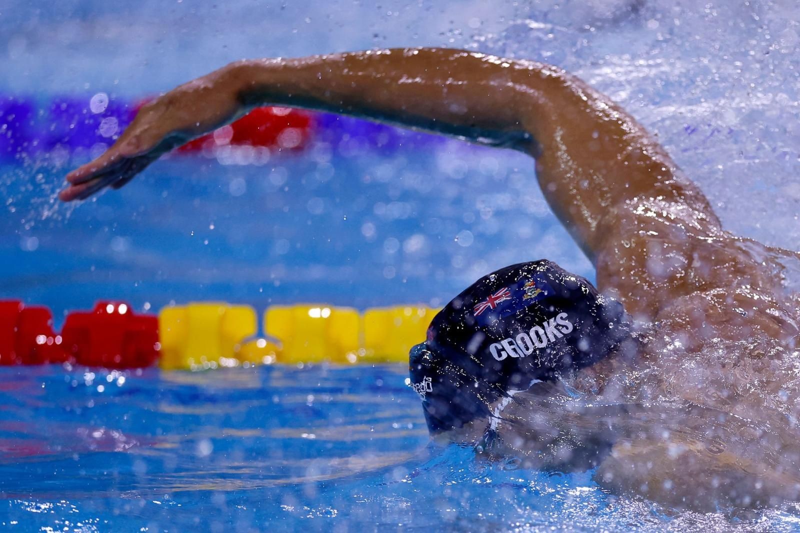 Swimmer performing freestyle stroke in a pool, arm extended above water with cap and goggles visible.